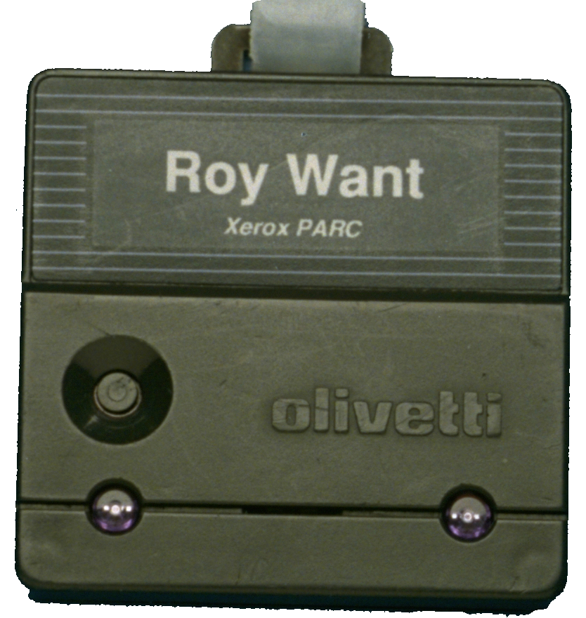 Olivetti Active Badge worn by Roy Want at Xerox PARC, showing a small rectangular device with infrared transmitter window and name badge, representing one of the earliest ubiquitous computing location-sensing devices from the early 1990s