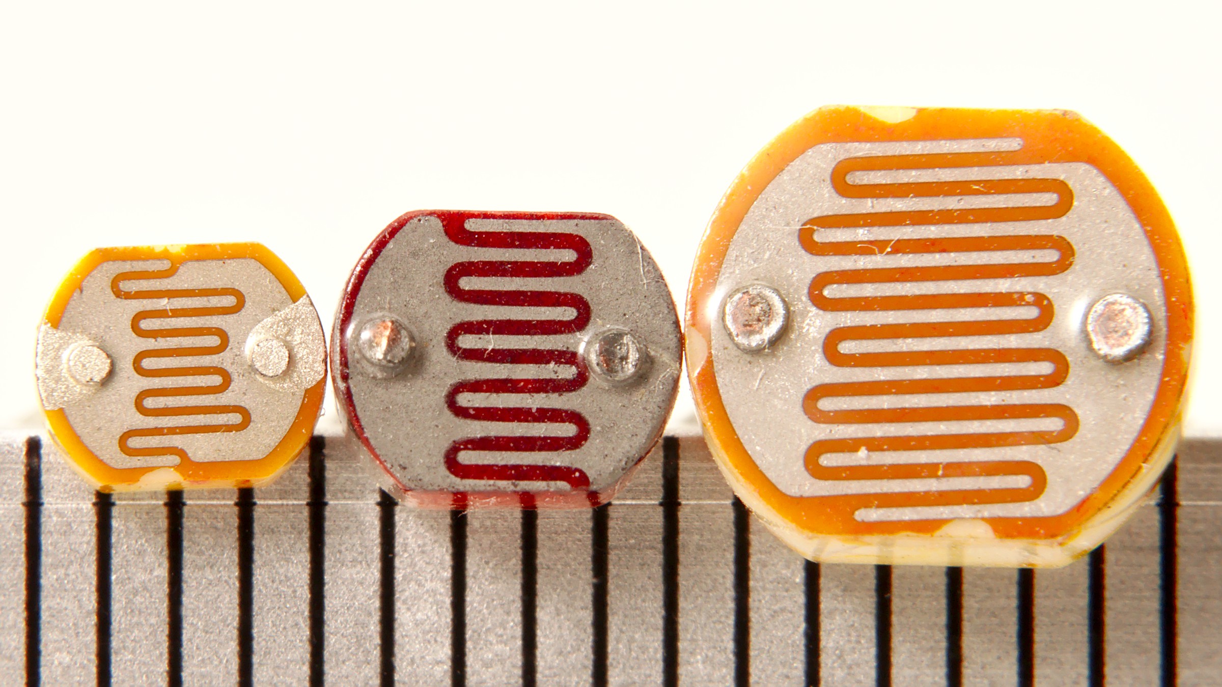 Close-up photograph of light dependent resistor LDR photoresistor component showing circular light-sensitive element with characteristic zigzag pattern of cadmium sulfide material between two wire leads, commonly used in smart lighting and ambient light sensing applications